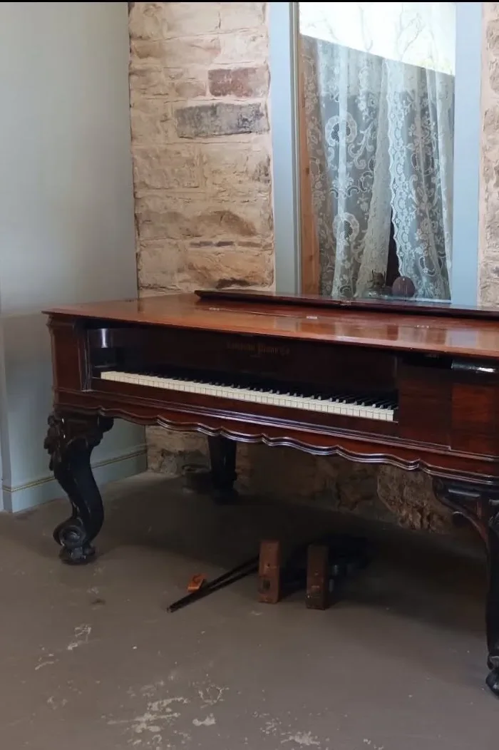 Emerson square grand piano beside a stone wall and lace curtains