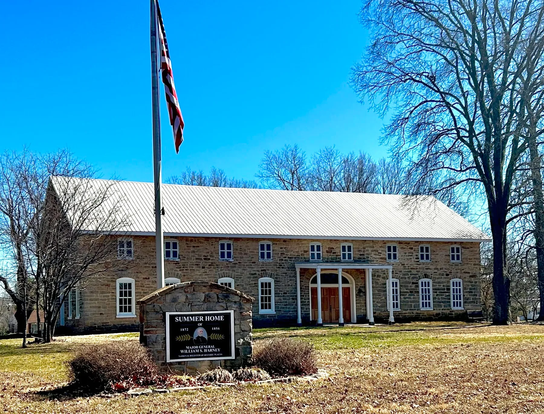 The Harney Mansion's long sandstone front with white porch, flag and Summer Home sign on a clear day